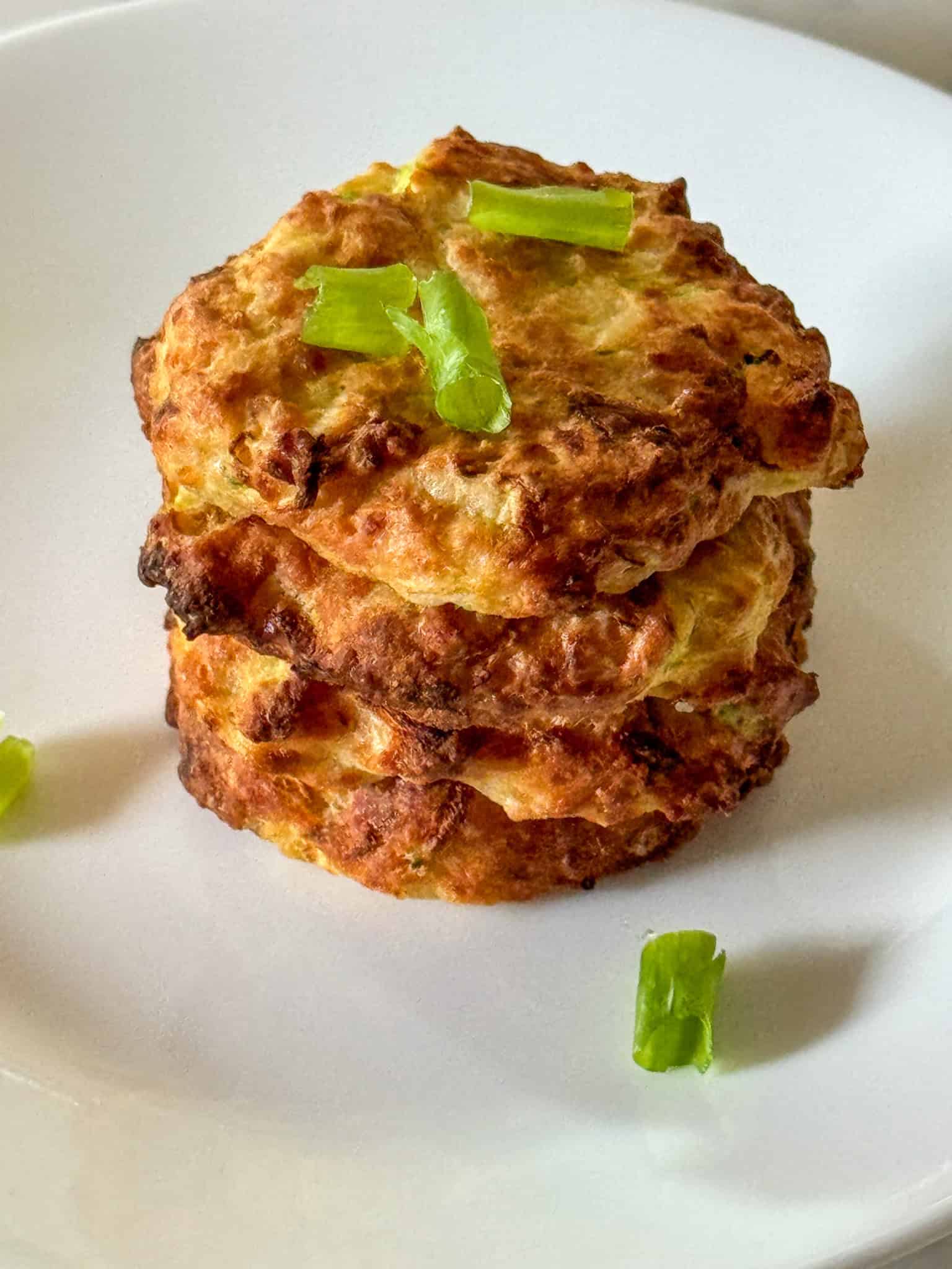 stack of four zucchini squash air fryer fritters garnished with green onion