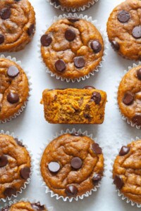 Image of half eaten vegan pumpkin muffin in the middle of a batch of other freshly baked pumpkin muffins