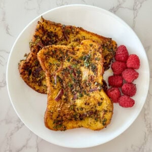 Two pieces of savory french toast served along side with raspberries on a white plate