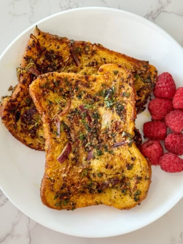 Two pieces of savory french toast served along side with raspberries on a white plate