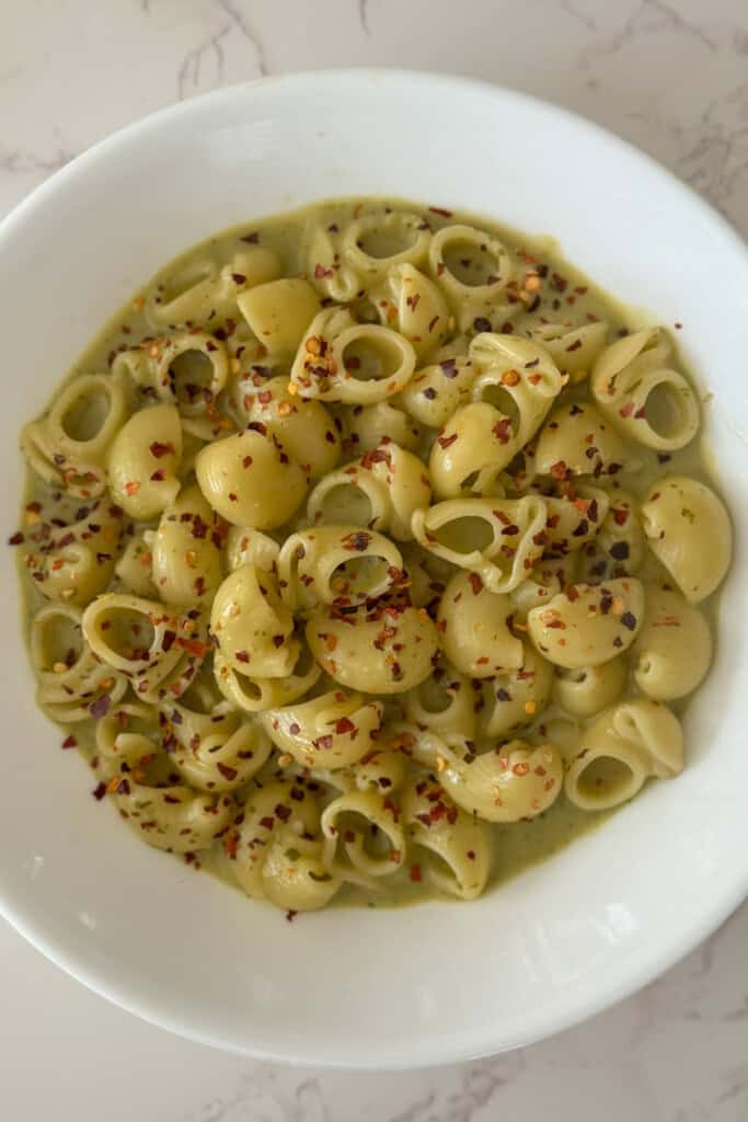 Elbow Pasta served in pesto cottage cheese pasta sauce sprinkled with red chili flakes in a white bowl