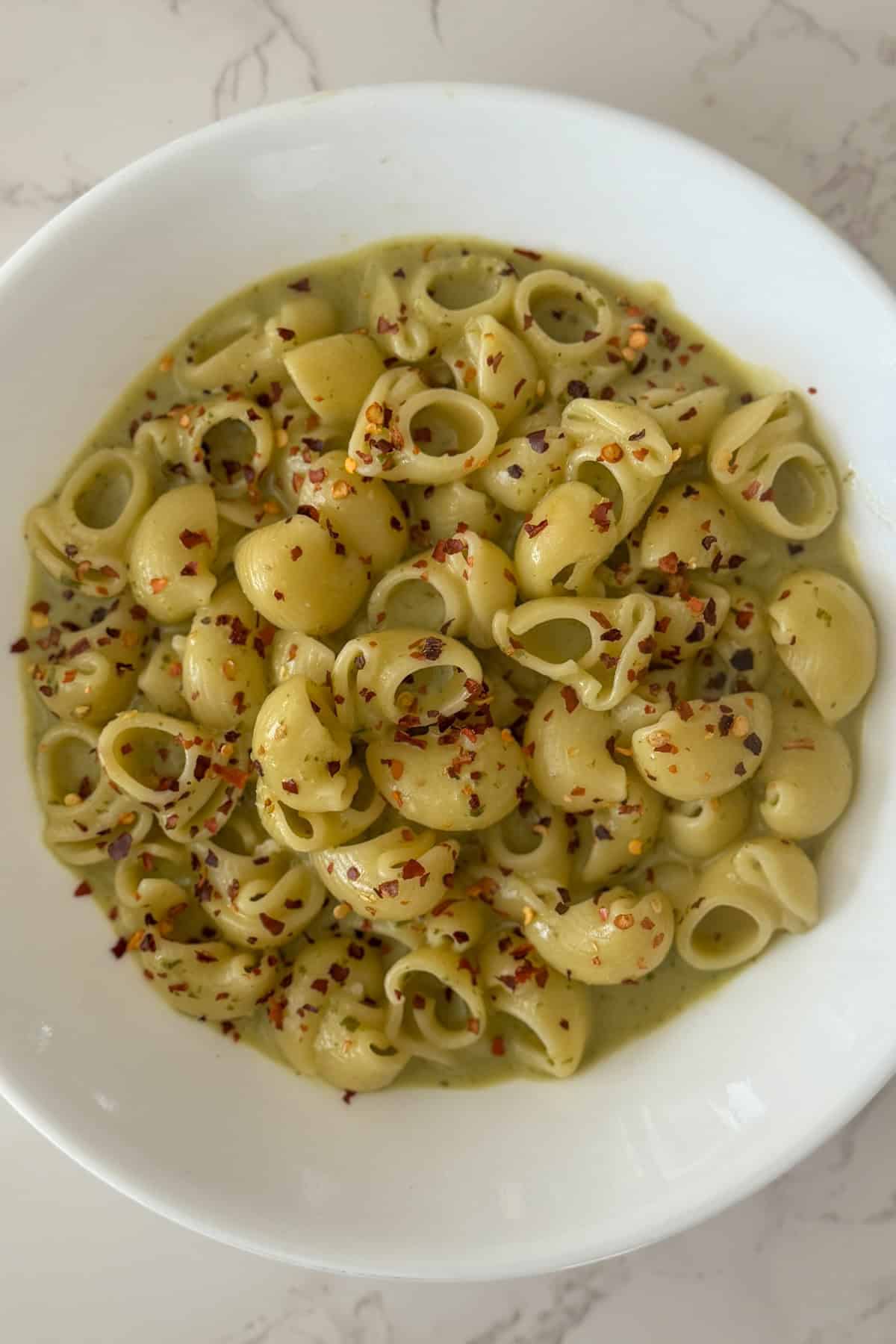 Elbow Pasta served in pesto cottage cheese pasta sauce sprinkled with red chili flakes in a white bowl