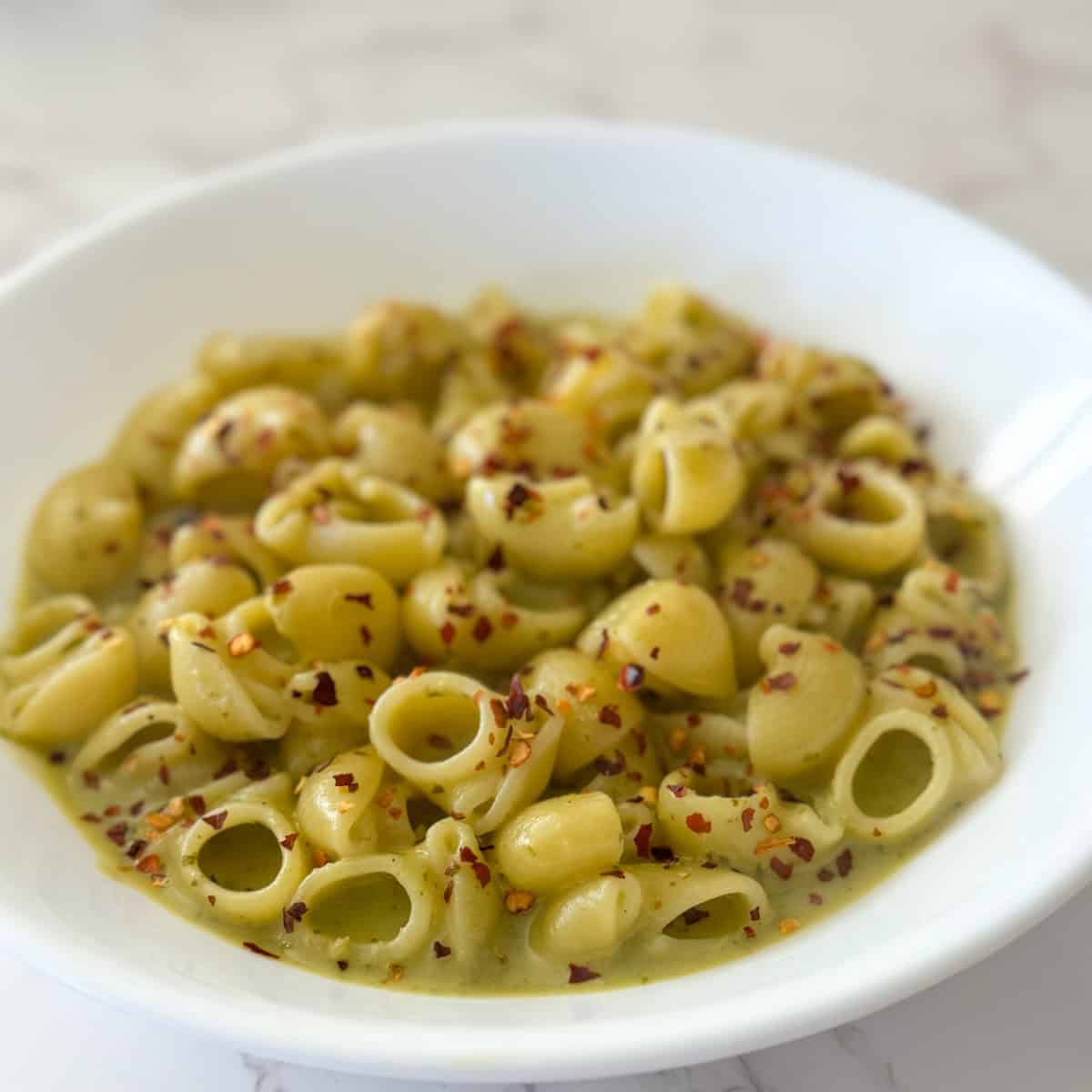 Pesto Cottage Cheese pasta sauce served on a white plate with crushed red chili flakes sprinkled on top