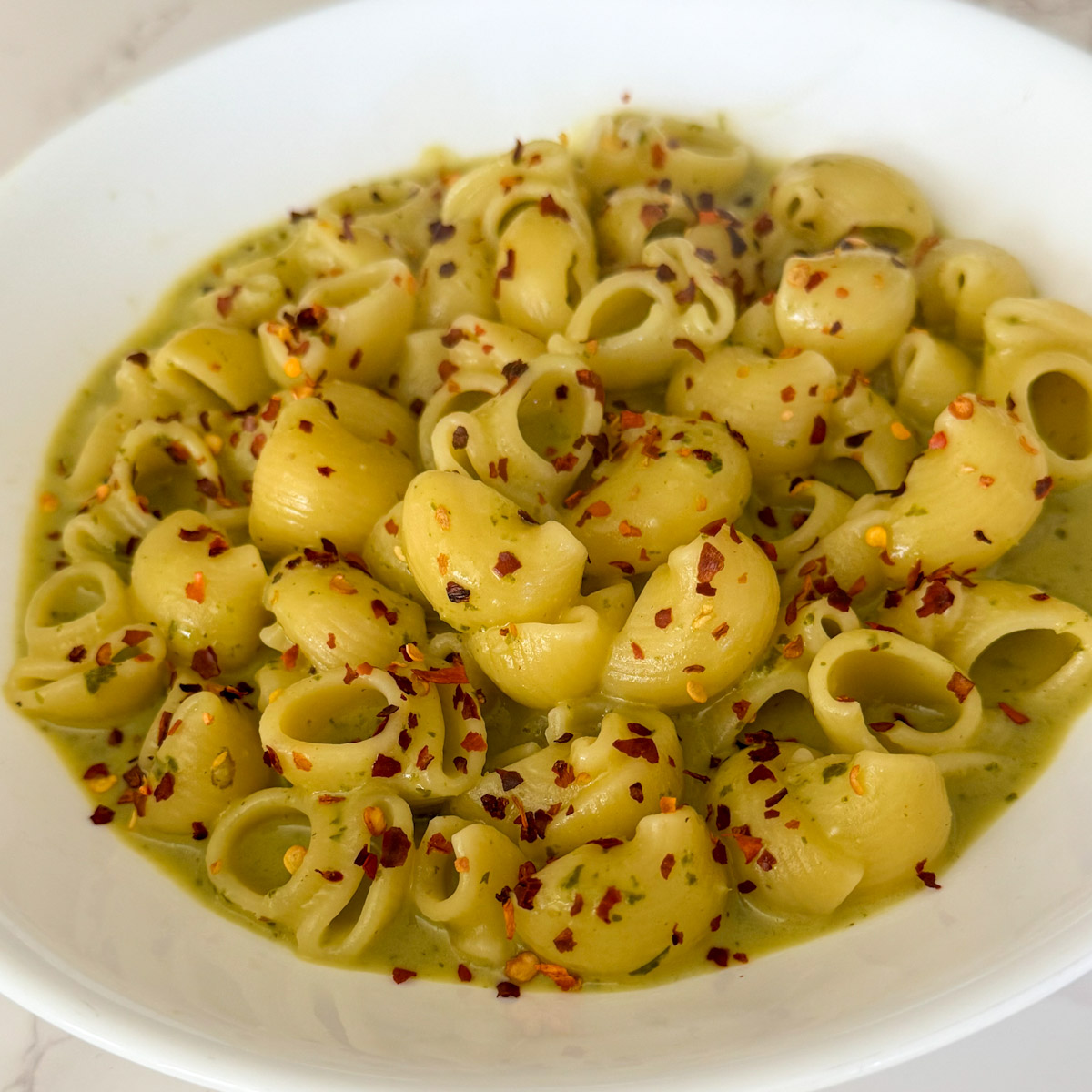 Cottage Cheese Pesto Pasta plated with crushed red chili flakes garnished on top